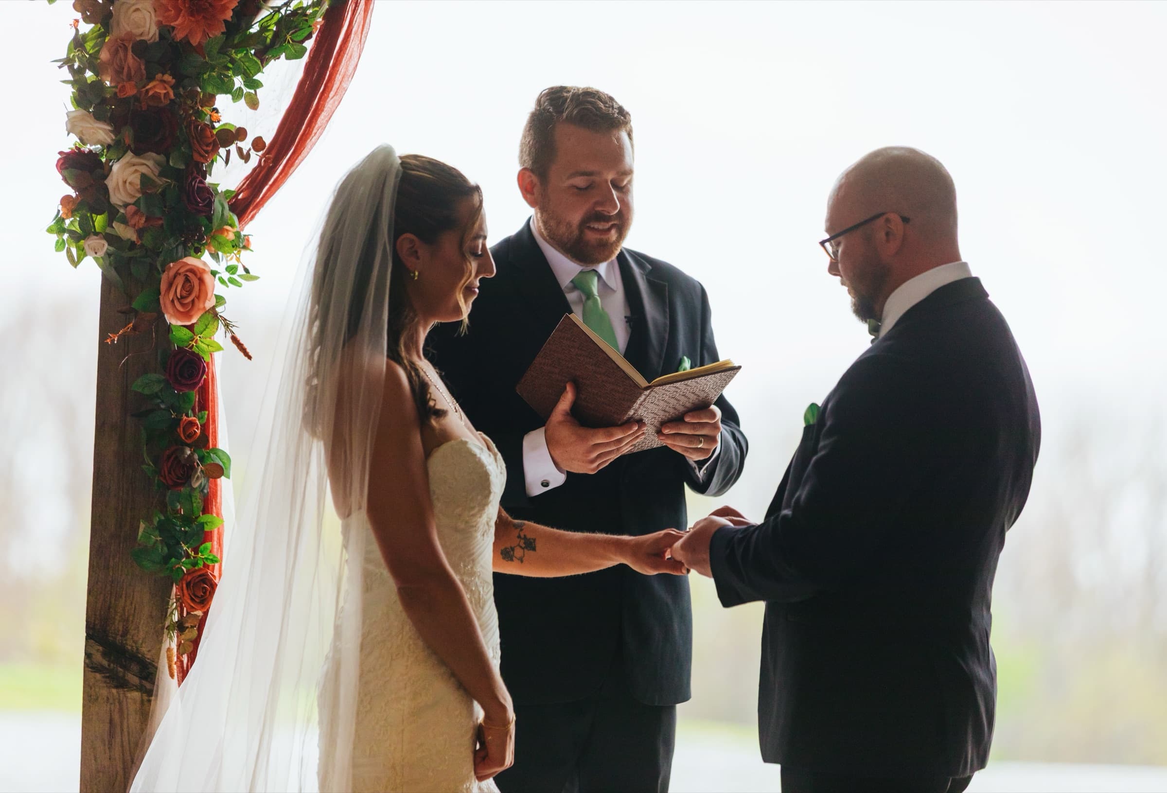Tight portrait of Jami and JJ exchanging rings under a floral arch